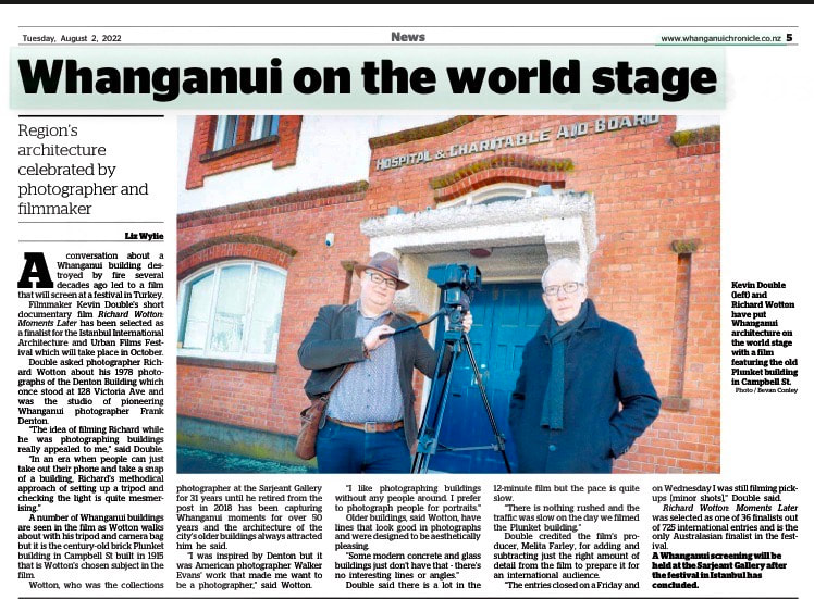 Whanganui on the world stage - a story from the Whanganui Chronicle printed edition on Tuesday 2nd August 2022. The story is about the film Richard Wotton: Moments Later and features a large photograph taken by Bevan Conley of filmmaker Kevin Double and photographer Richard Wotton standing outside the Plunket building in Campbell Street, Whanganui. Kevin is wearing a brown brimmed hat, patterned shirt, and green casual suit jacket. He has a leather shoulder bag on and is holding onto a high tripod and with camera equipment on top. Richard is wearing a dark coloured overcoat and scarf. Both are looking into the camera. The words Hospital & Charitable And Board, made in chunky concrete letters, are visible on the red brick building behind them above the stippled white concrete of the blue doorway.  All Rights Reserved NZME Whanganui Chronicle, used here under fair use terms.